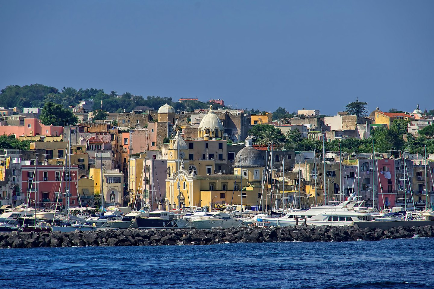 Colorati edifici di città mediterranea salgono su una collina che domina un porto.