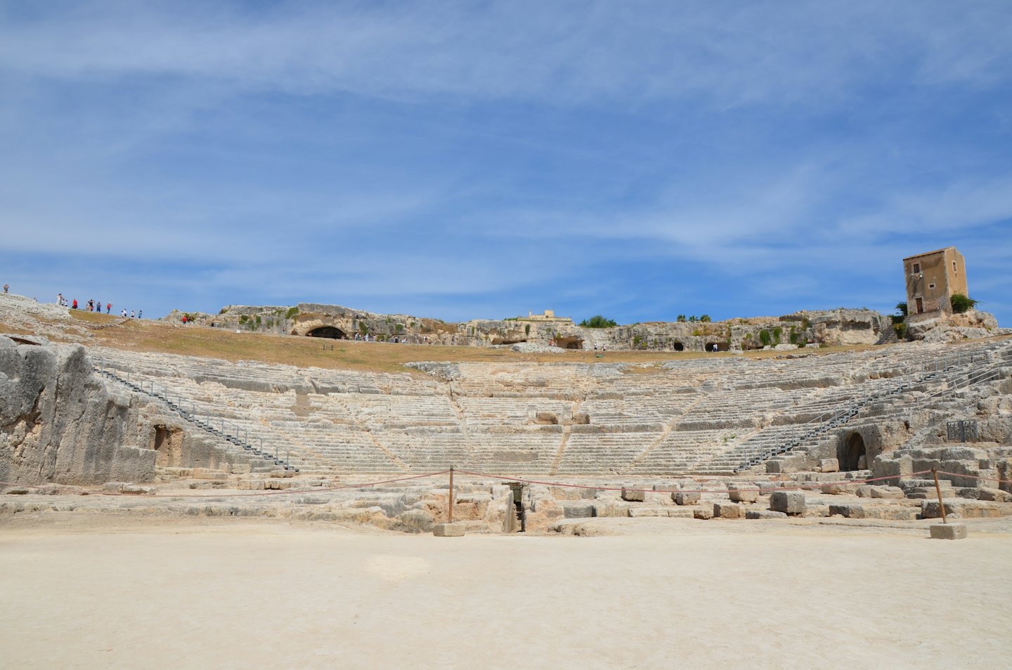 Turisti esplorano le gradinate di un antico teatro greco.