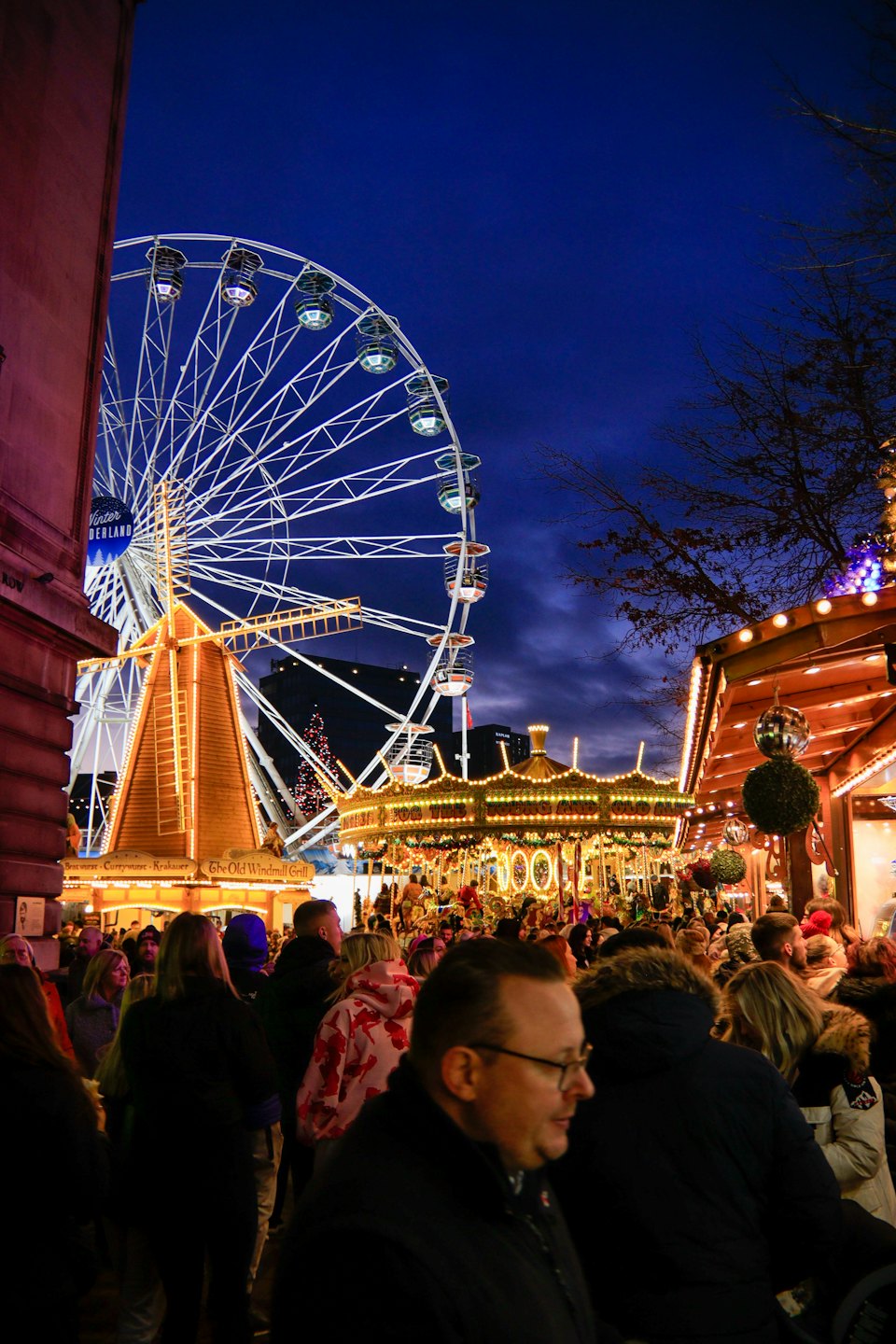 Folla passeggia in un mercato notturno festivo con ruota panoramica.