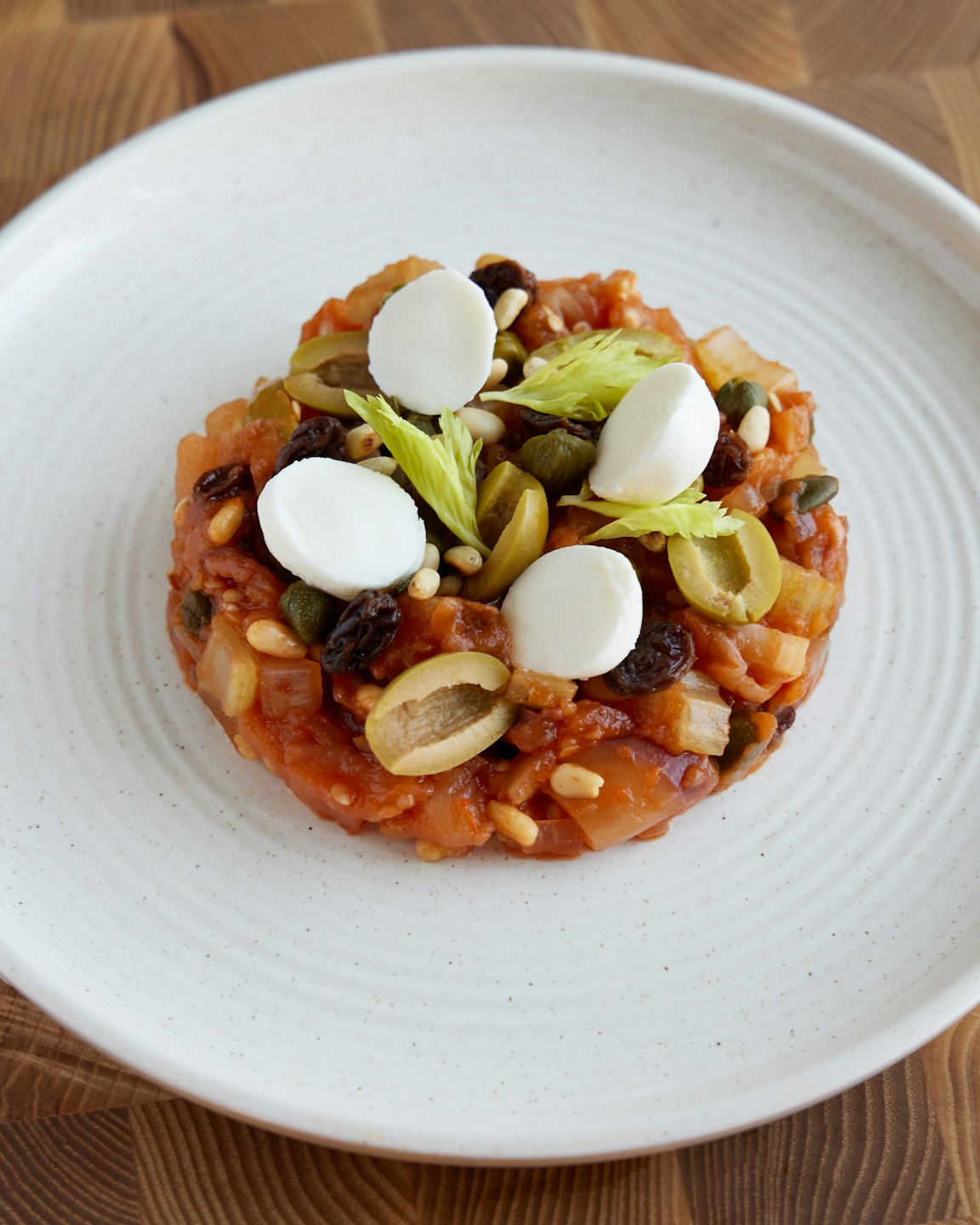 Caponata di pomodoro e verdure su piatto bianco con mozzarella.