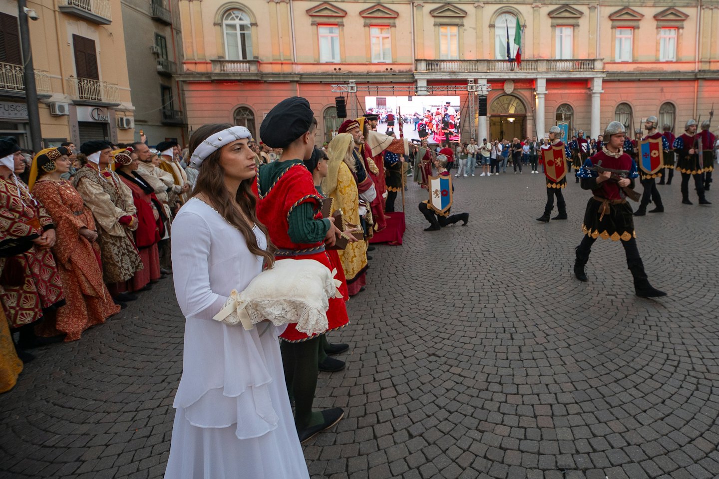 Artisti in costume partecipano a una parata in una piazza acciottolata.
