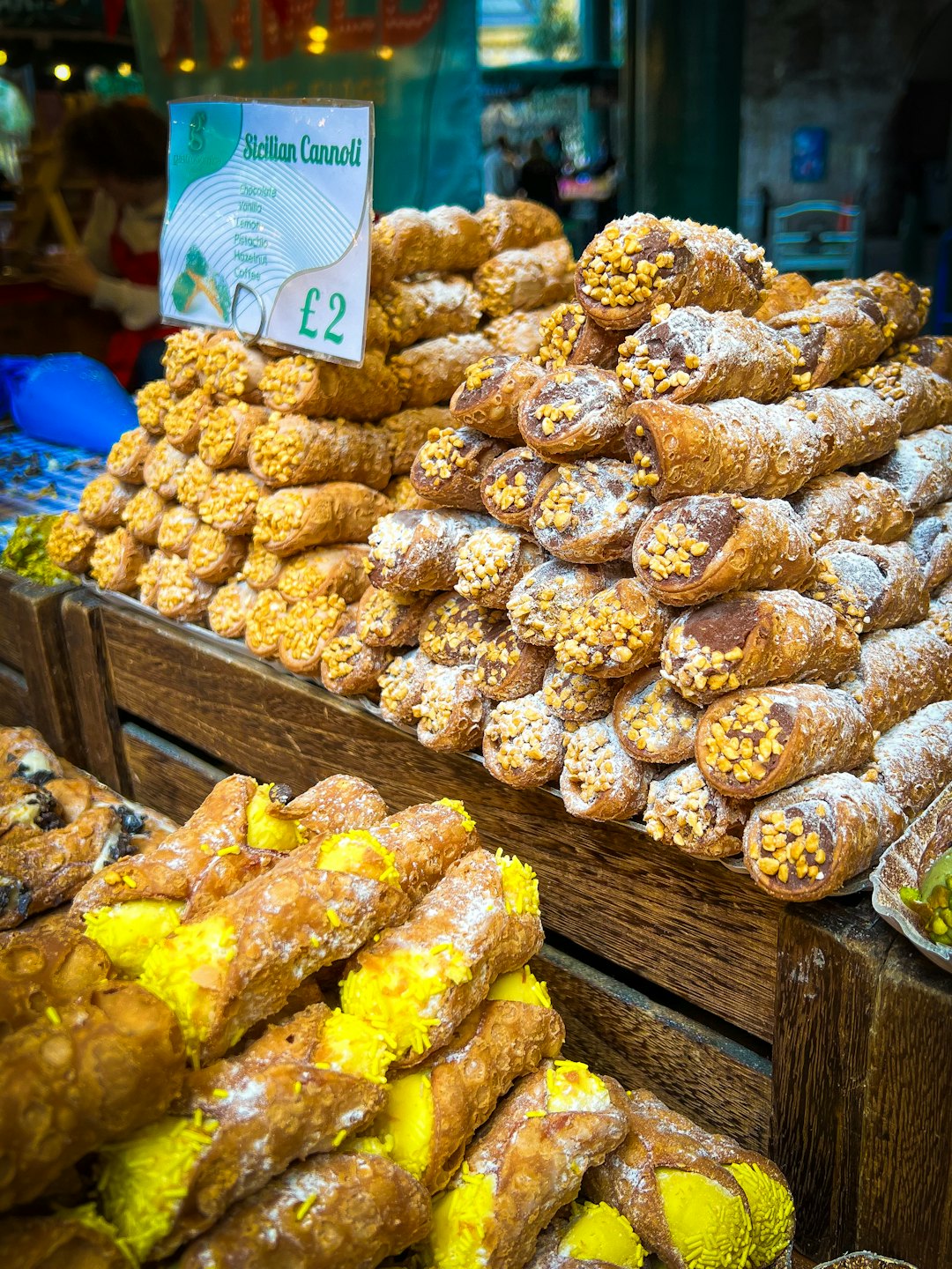 Pila di cannoli siciliani ripieni su un banco di mercato in legno.